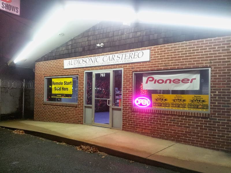 Brick storefront after dark with Pioneer banner and neon open sign at AudioSonic Car Stereo in Brooklawn, New Jersey