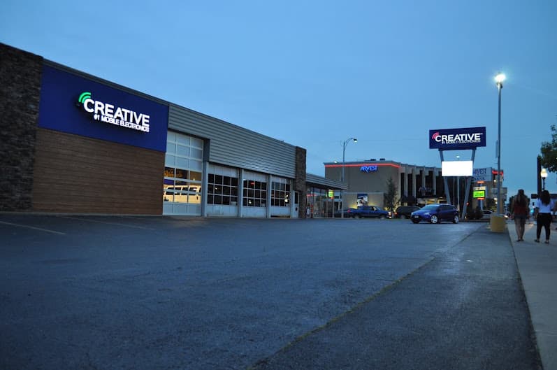 Storefront with blue sign over parking lot in evening light at Creative Audio in Joplin, Missouri