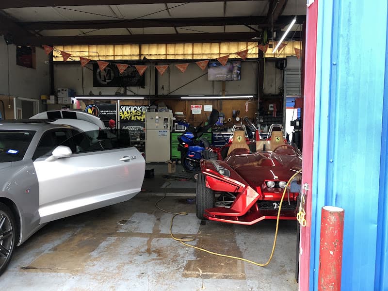 Silver coupe and red three-wheel roadster parked in a shop bay at Unlimited Car Stereo in Houston, Texas