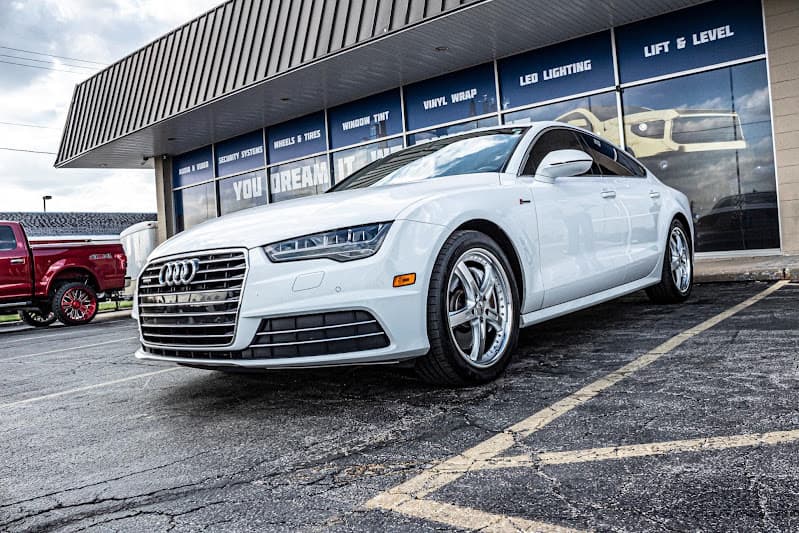 White Audi car parked in front of a window with service signs at Custom Audio Creation in Independence, Missouri