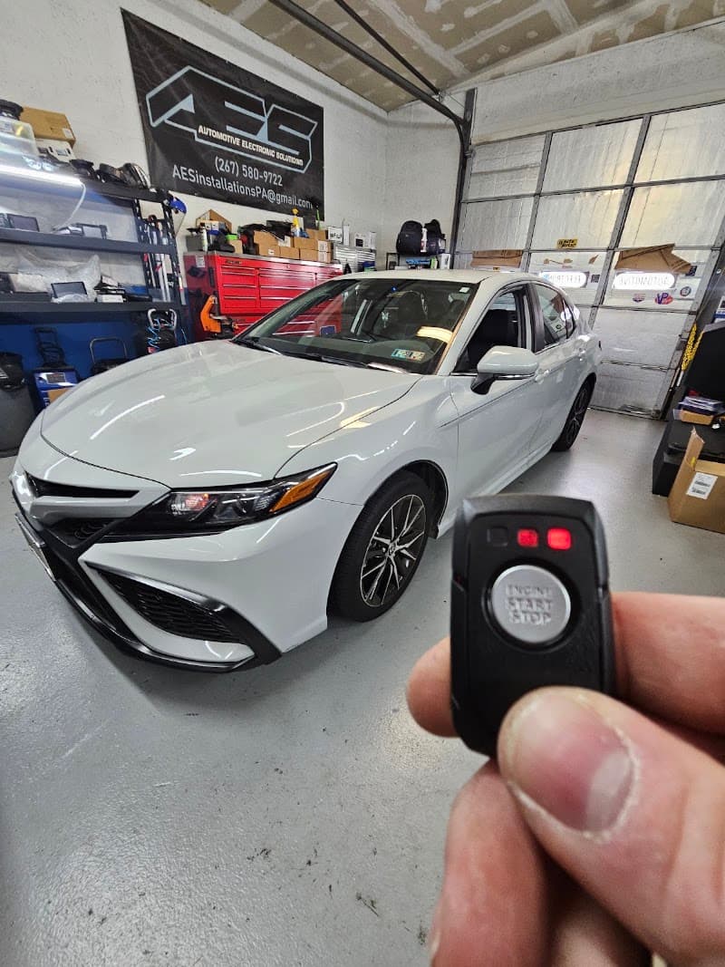 Remote start key fob held up in front of a white sedan at Automotive Electronic Solutions in Levittown, Pennsylvania