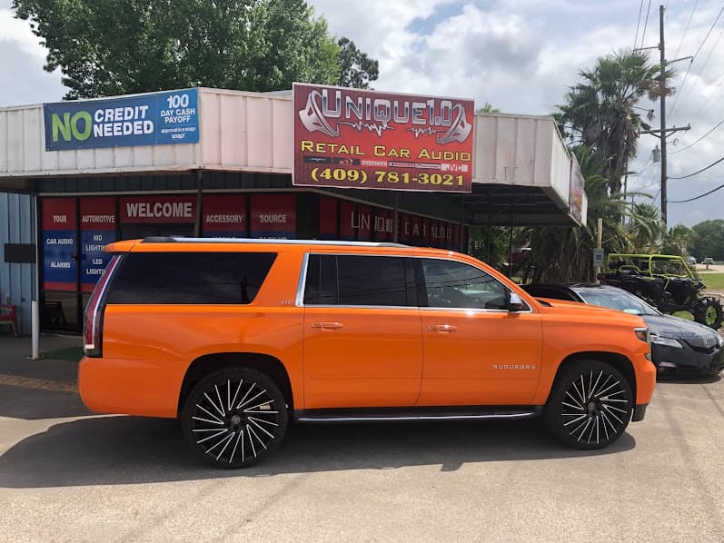 Orange Suburban SUV with black wheels parked outside storefront at Unique 1.0 Car Audio in Beaumont, Texas