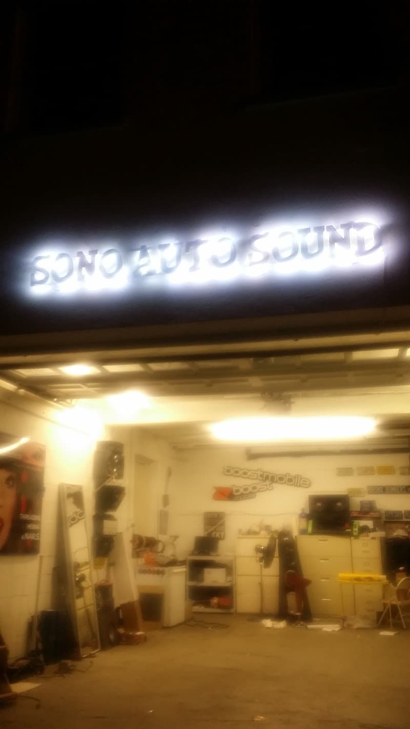 Glowing white sign above an open garage bay after dark at Sono auto sound in Norwalk, Connecticut