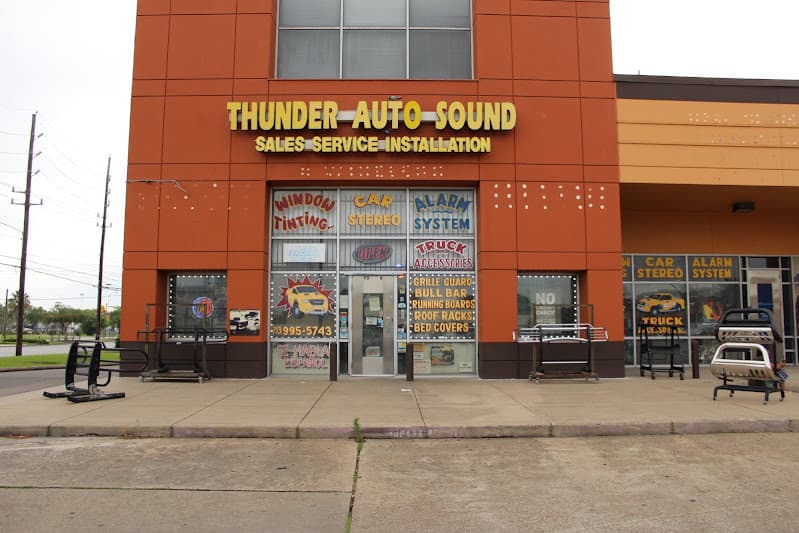 Wide view of orange storefront with glass entrance and window signs at Thunder Auto Sound in Houston, Texas