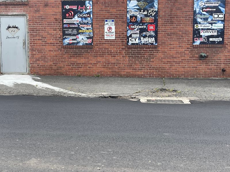 Brick wall with banners of audio brand logos beside a gray door at Diamond Audio CiTy in New Britain, Connecticut