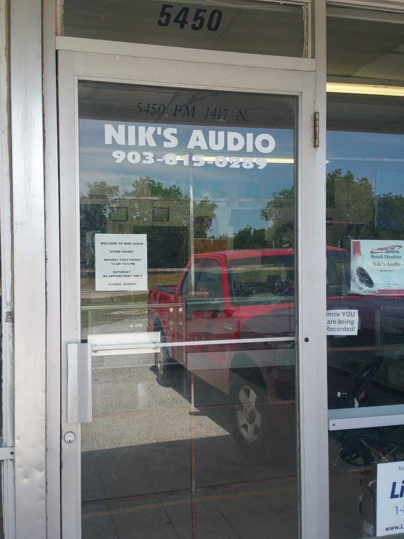 Glass shop door with white lettering and store hours sign at Niks Audio in Sherman, Texas