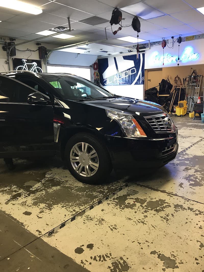 Black SUV parked in a garage below a JL Audio banner at AT Audio in Denver, Colorado