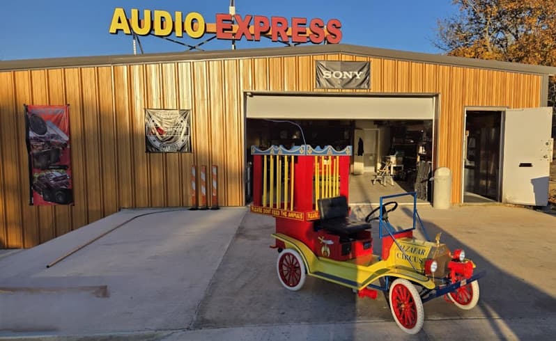 Red and yellow vintage-style car with a cage body outside a shop at Audio Express in Floresville, Texas