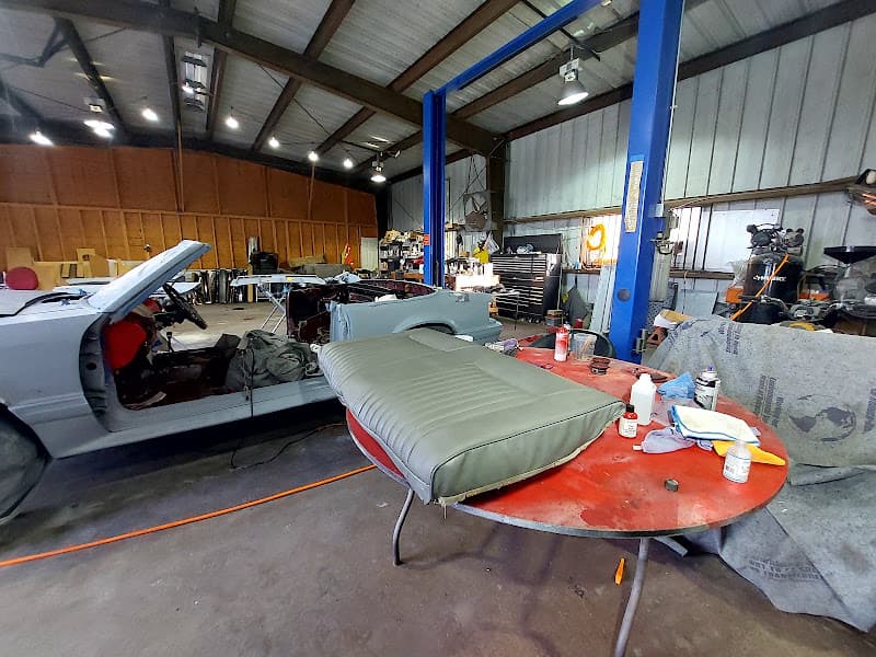Garage with blue lift, gray car body and seat cushion on red table at Autoworkz by Dmac in Fresno, Texas
