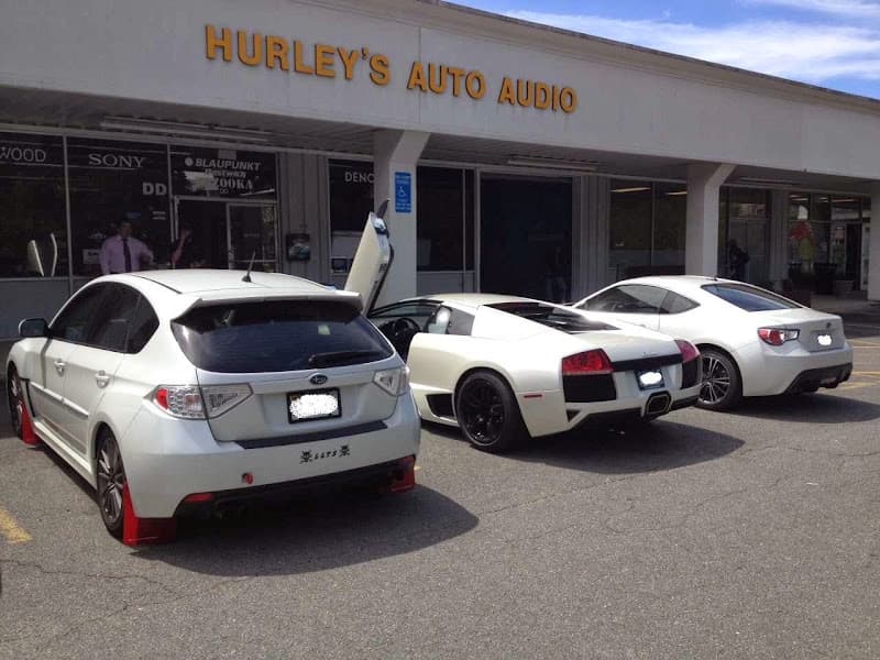Storefront with white hatchback and white sports coupe parked outside at Hurley's Auto Audio in McLean, Virginia