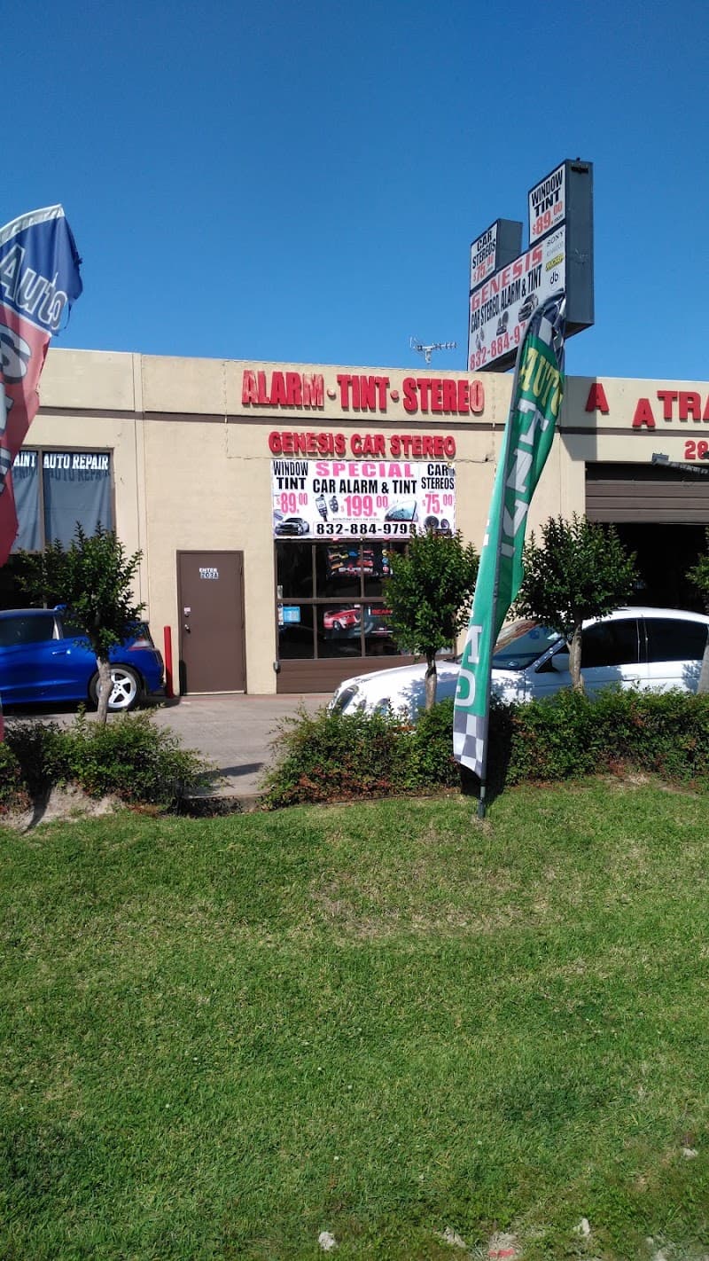 Beige storefront with red Alarm Tint Stereo sign and flags at Genesis Car Stereo in Houston, Texas