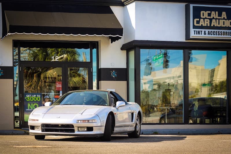 Silver sports coupe parked outside a shop with dark window frames at Ocala Car Audio and Tint in Ocala, Florida