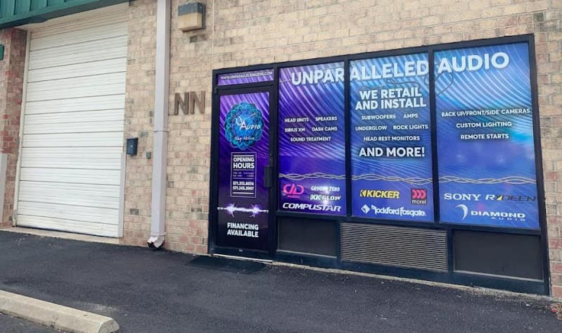 Brick storefront with roll-up door and large window graphics at Unparalleled Audio in Sterling, Virginia