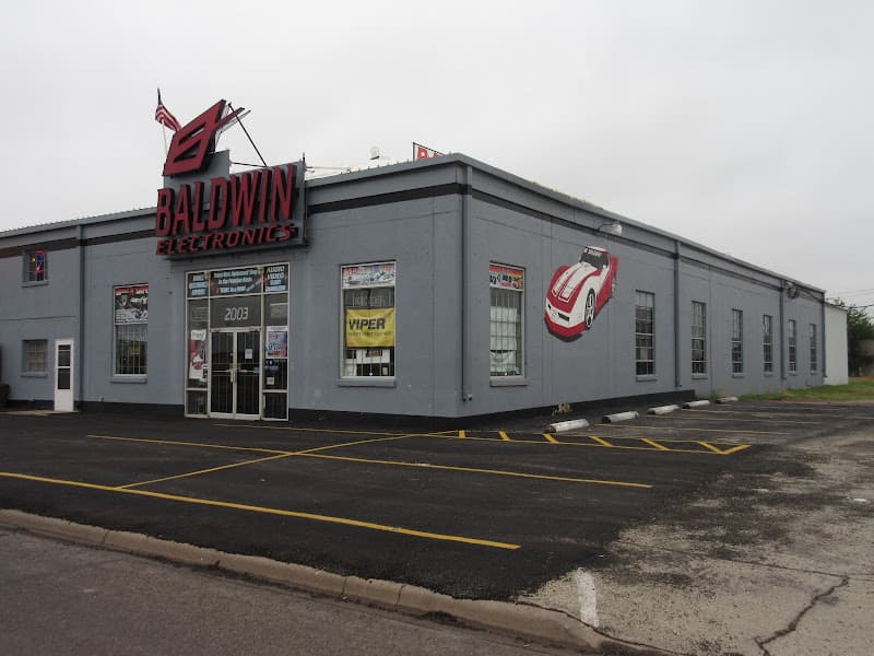Grey storefront with red roof sign and empty parking lot at Baldwin Electronics in Odessa, Texas