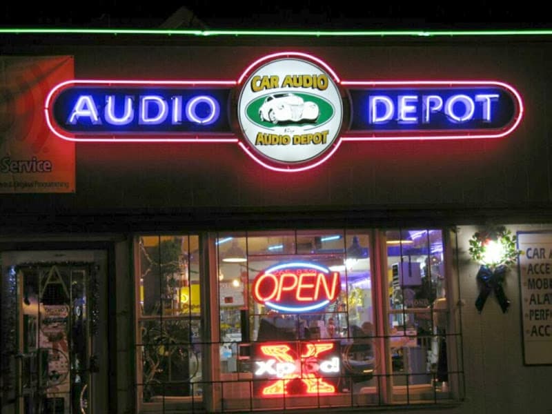 Neon OPEN and logo signs on storefront after dark at Audio Depot - Car Audio & Alarm in Mount Holly, New Jersey