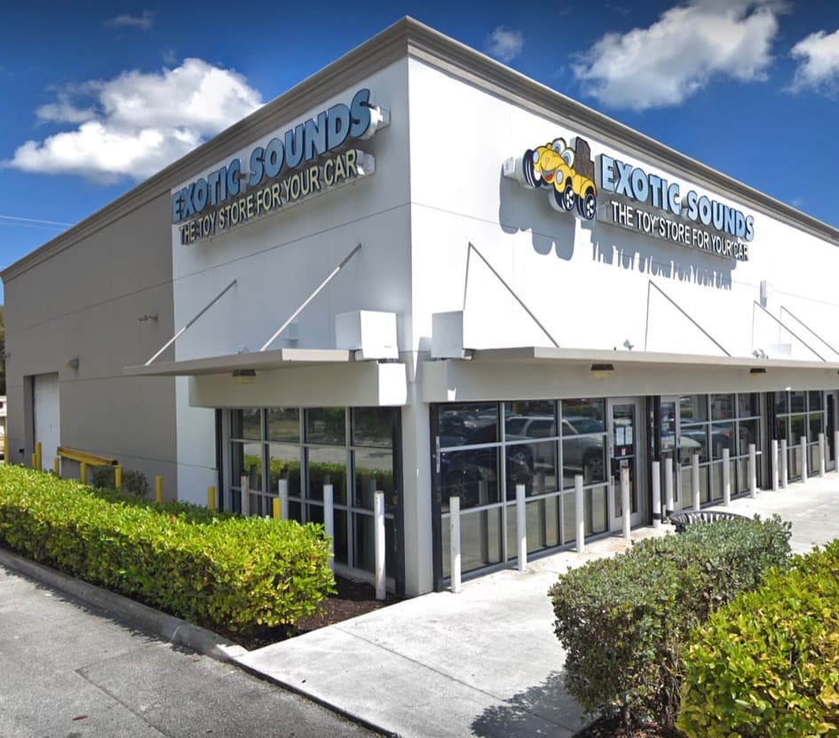White storefront with blue sign and yellow cartoon car logo at Exotic Sounds Inc in Cutler Bay, Florida