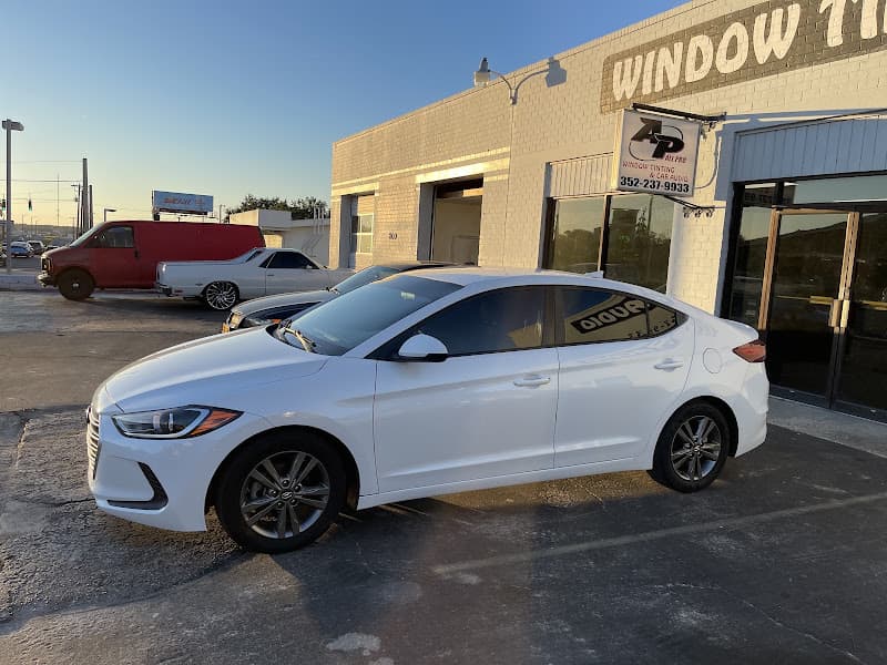 White sedan parked in front of a brick shop at All Pro Window Tint & Car Audio in Ocala, Florida