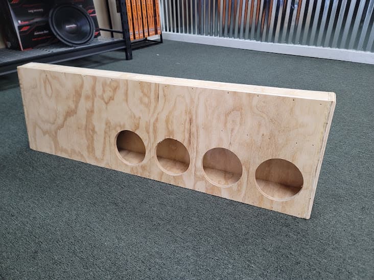 Unfinished plywood box with four round openings on carpet at Beat Down Car Audio in Hammond, Louisiana
