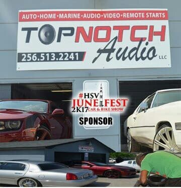 Banner sign for auto and marine audio above a shop with parked cars at Top Notch Audio LLC in Huntsville, Alabama