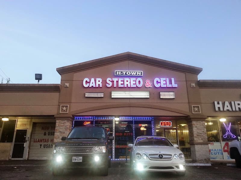 Lit storefront with Car Stereo and Cell sign and two parked cars at H-Town Mobile Audio in Houston, Texas