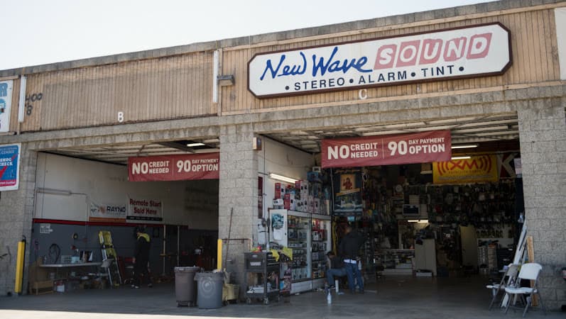 Open shop bays with red banners and a sign above the entrance at New Wave Sound in Gardena, California