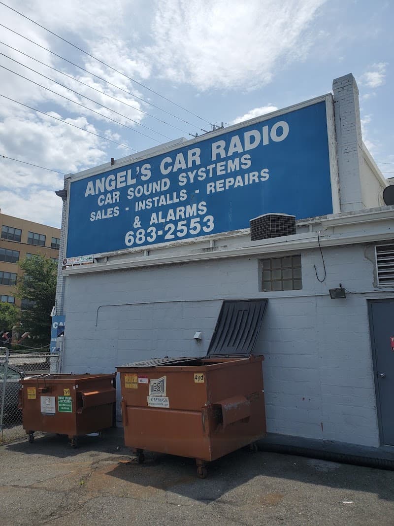 Blue wall sign with white lettering above two dumpsters at Angelos Car Radio LLC in Alexandria, Virginia
